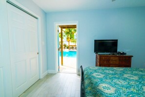 A bedroom with a bed, a TV on a wooden dresser, and a door leading to a pool area.