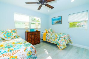 A bedroom with two beds, a ceiling fan, a dresser, and a painting on the wall.