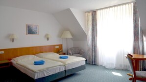 Habitación de hotel con dos camas, una silla, una mesa, una lámpara y un cuadro en la pared.