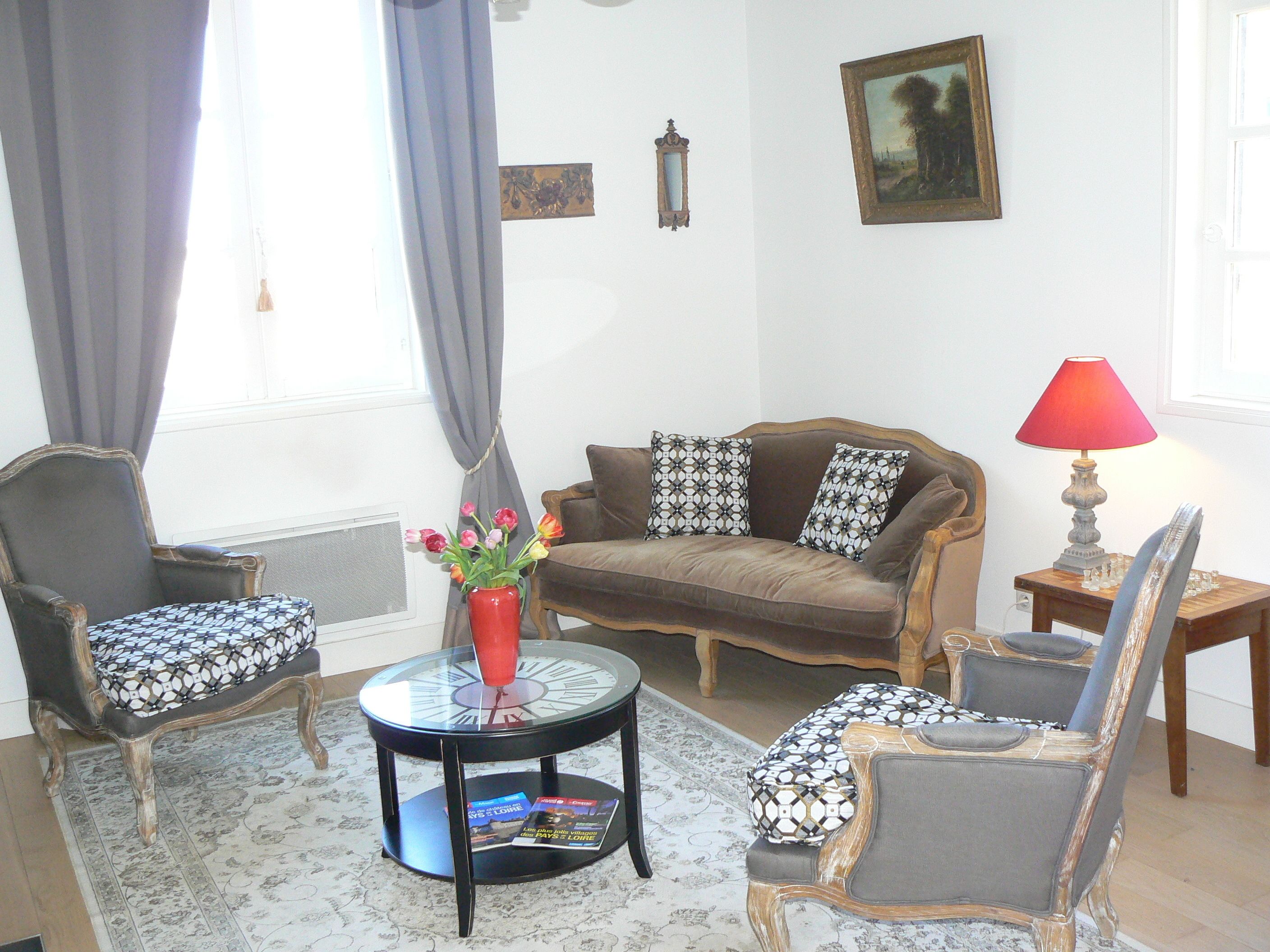 A living room with a brown sofa, patterned armchairs, a coffee table with a vase of flowers, a red lamp, and a painting on the wall.
