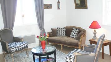 A living room with a brown sofa, patterned armchairs, a coffee table with a vase of flowers, a red lamp, and a painting on the wall.