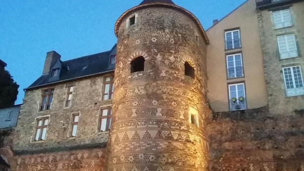 Een historisch stenen torentje met ingewikkelde patronen, naast een gebouw met meerdere ramen en een schuin dak.