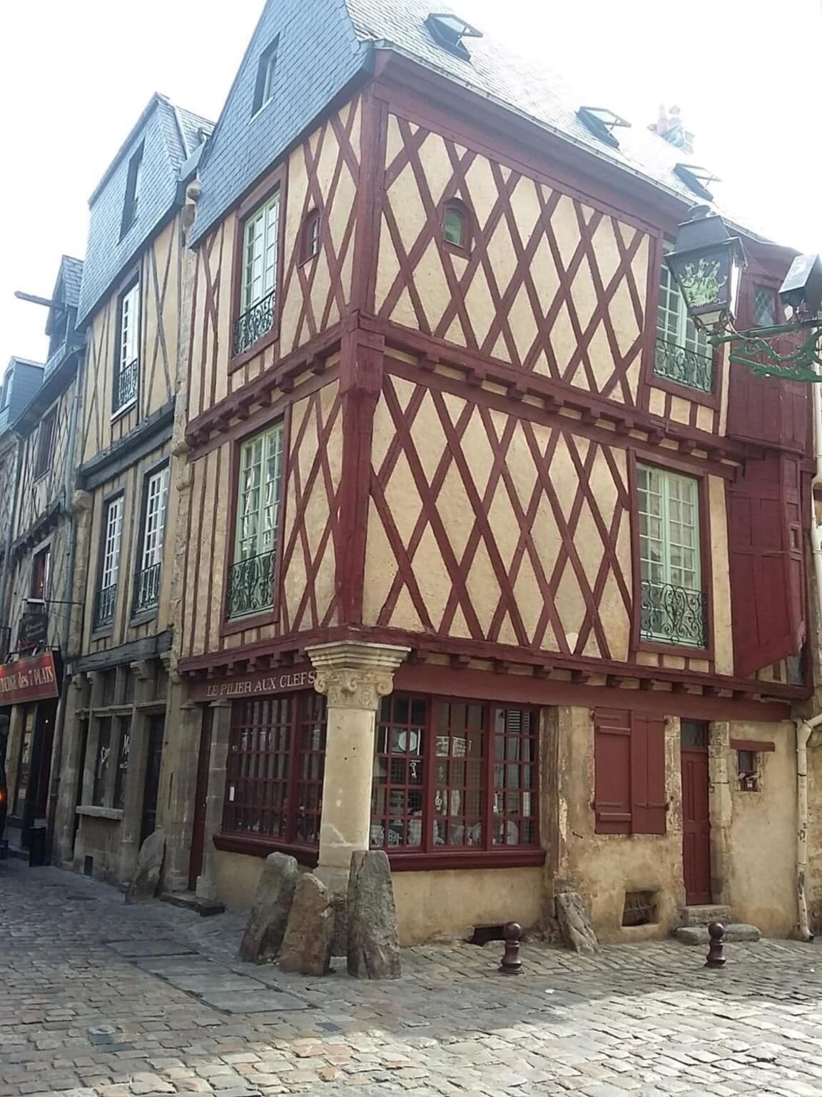 A traditional half-timbered building with a stone base and a wooden upper story, featuring a ground-floor shop with a sign reading "LE PILIER AUX CLEFS".
