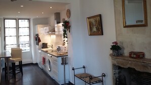 Een keuken met een ingebouwde wasmachine, een eethoek met een tafel en stoelen, een open haard en een grote spiegel aan de muur.