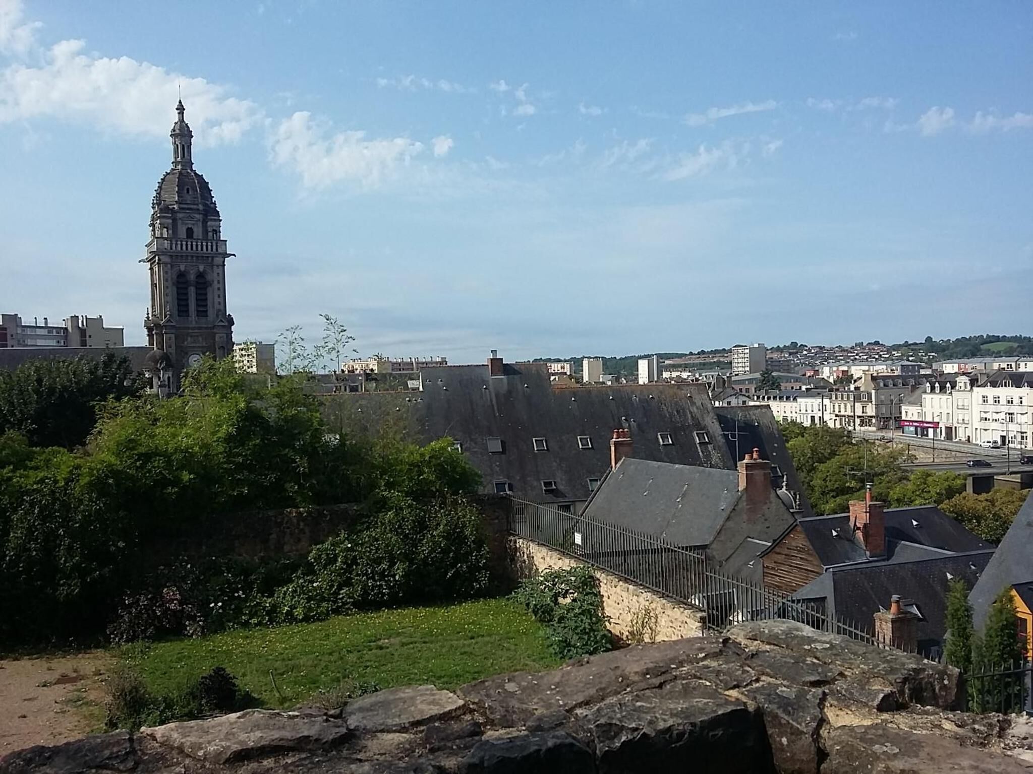 A view of a town with a prominent clock tower, surrounded by residential buildings and greenery.