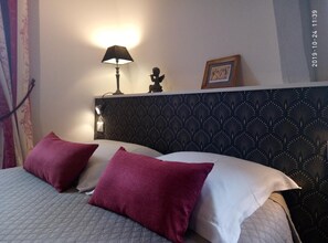 A hotel room with a bed, two pillows, a nightstand with a lamp, a framed picture, and a decorative headboard. - Appartement Relais Saint Pavin (Le Mans)