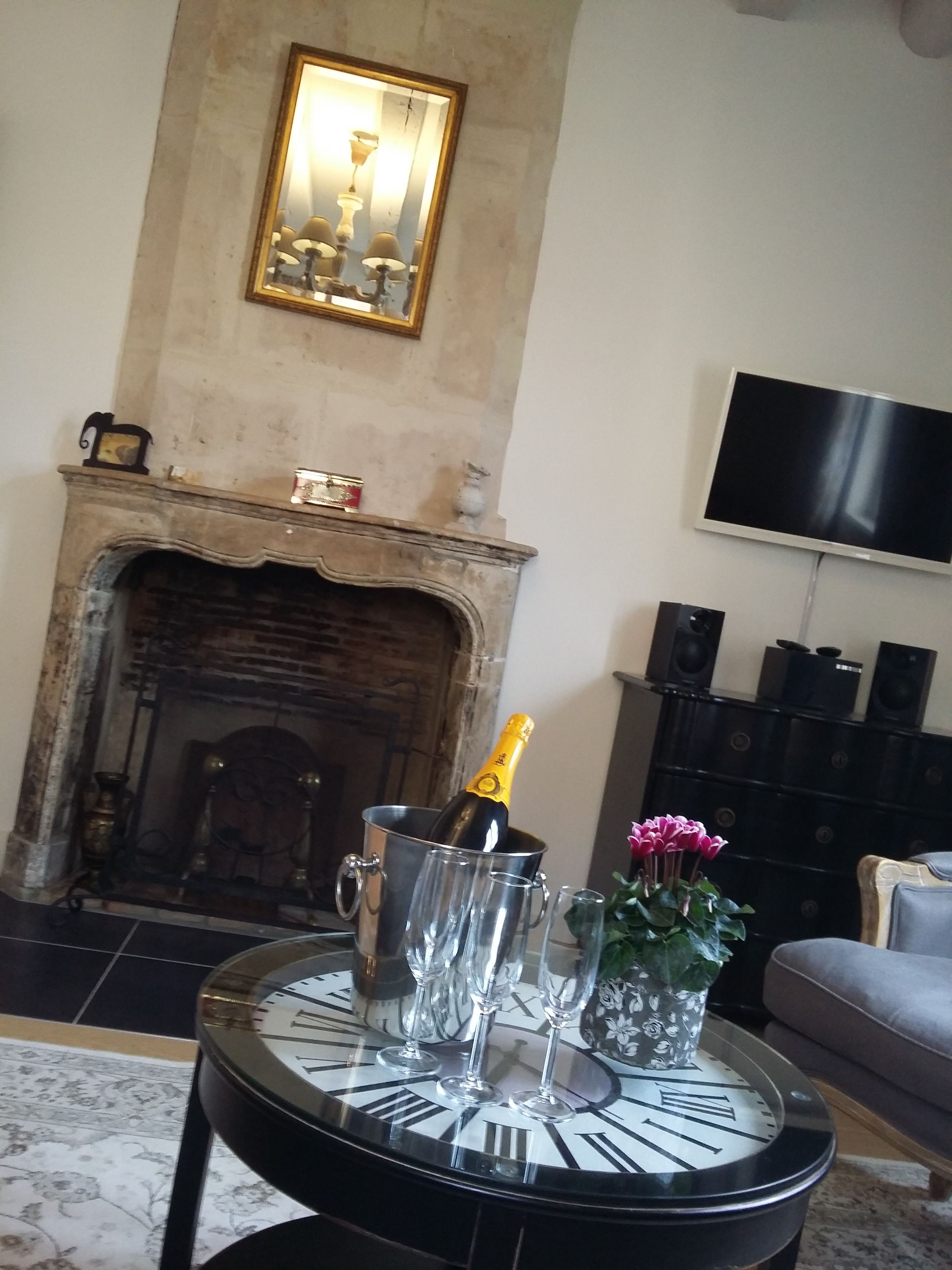 A living room with a fireplace, a clock table, a TV, and a speaker system.