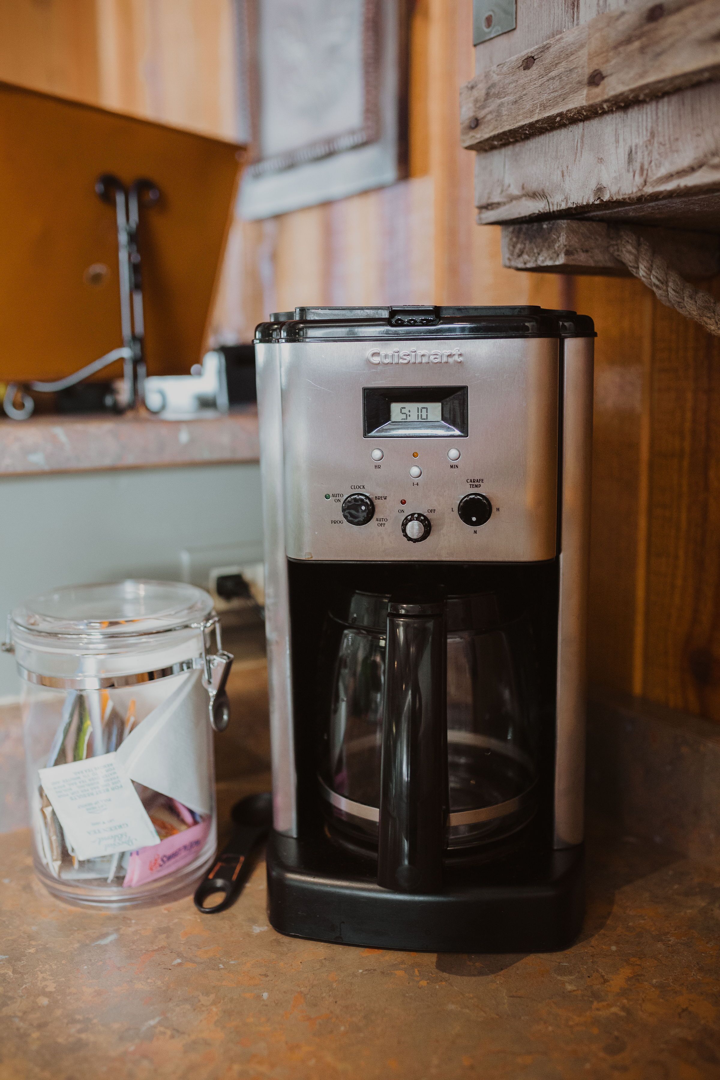 Une machine à café dotée d’un écran numérique, une cafetière et un bocal en verre avec une étiquette, le tout posé sur un plan de travail de cuisine.