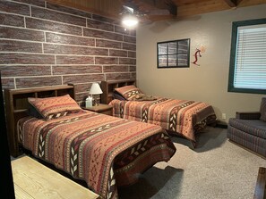 A room with two beds, a wooden headboard, a nightstand with a lamp, a window with blinds, and a chair. - Perfect for family gatherings, escapes, retreats or seasonal vacations (Pinetop)