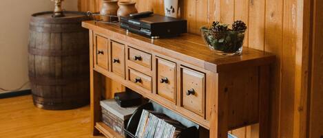 A wooden-paneled room with a television mounted on the wall, a wooden cabinet with drawers, a lamp, and a barrel.