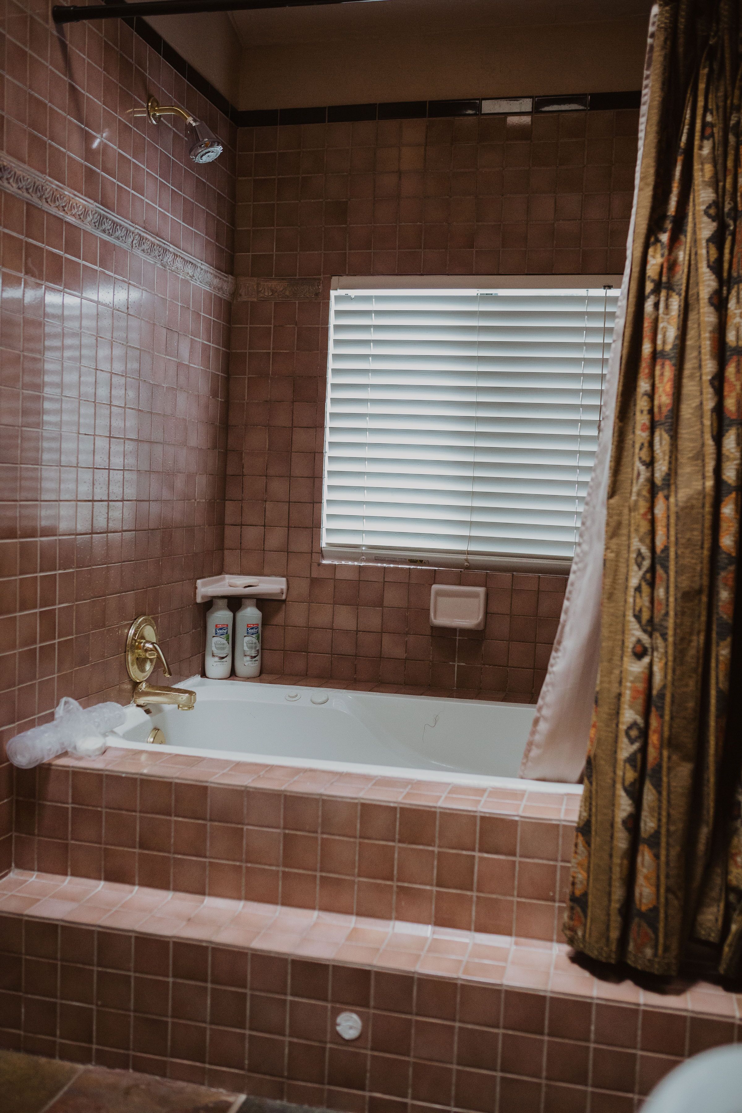 A bathroom with a bathtub, a showerhead, and a window with blinds.
