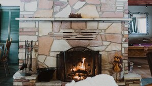 A stone fireplace with a fire, wooden beams, and a ceiling fan. - Perfect for family gatherings, escapes, retreats or seasonal vacations (Pinetop)