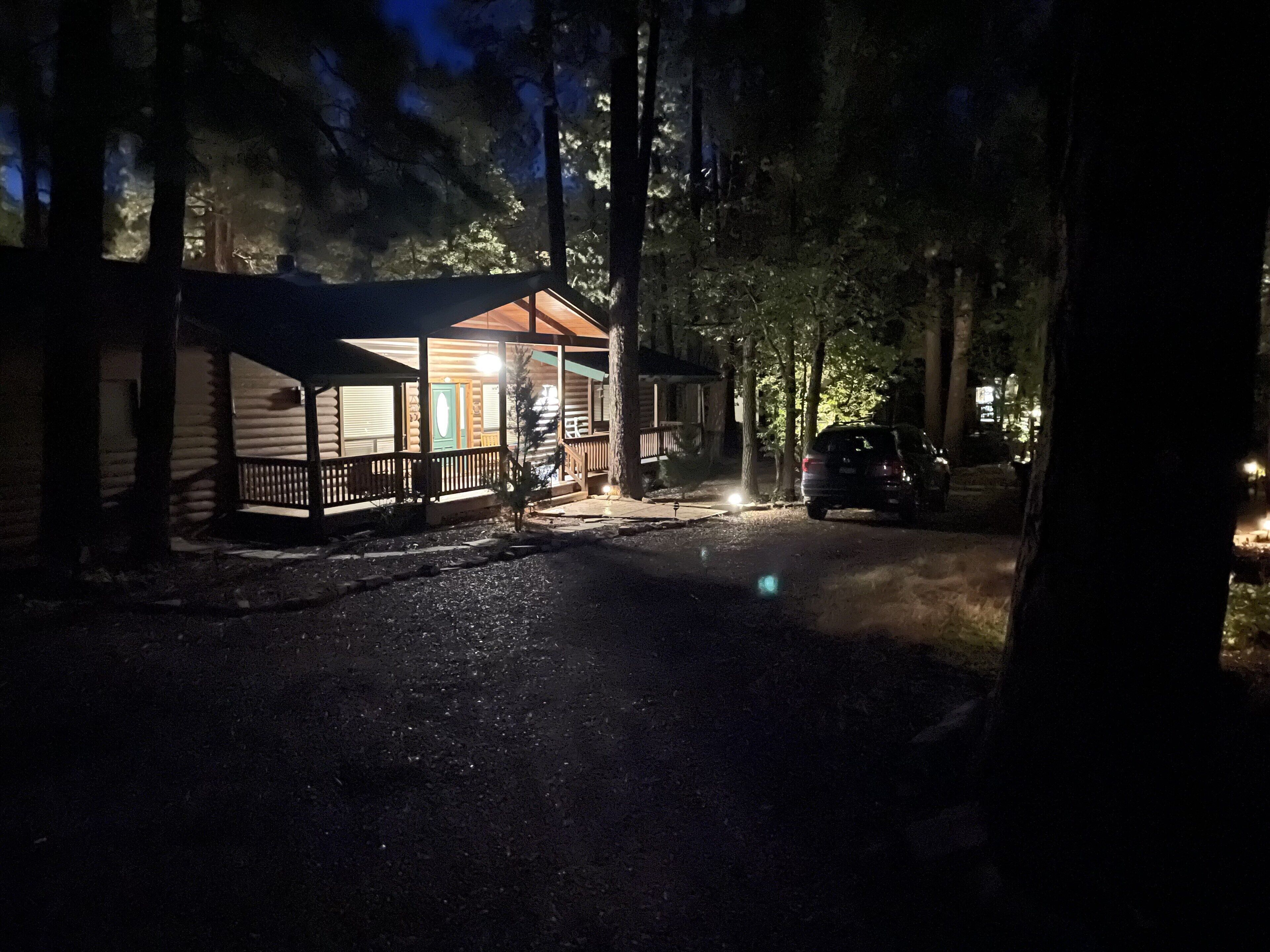 A cabin with a porch, a covered area, and a vehicle parked nearby.