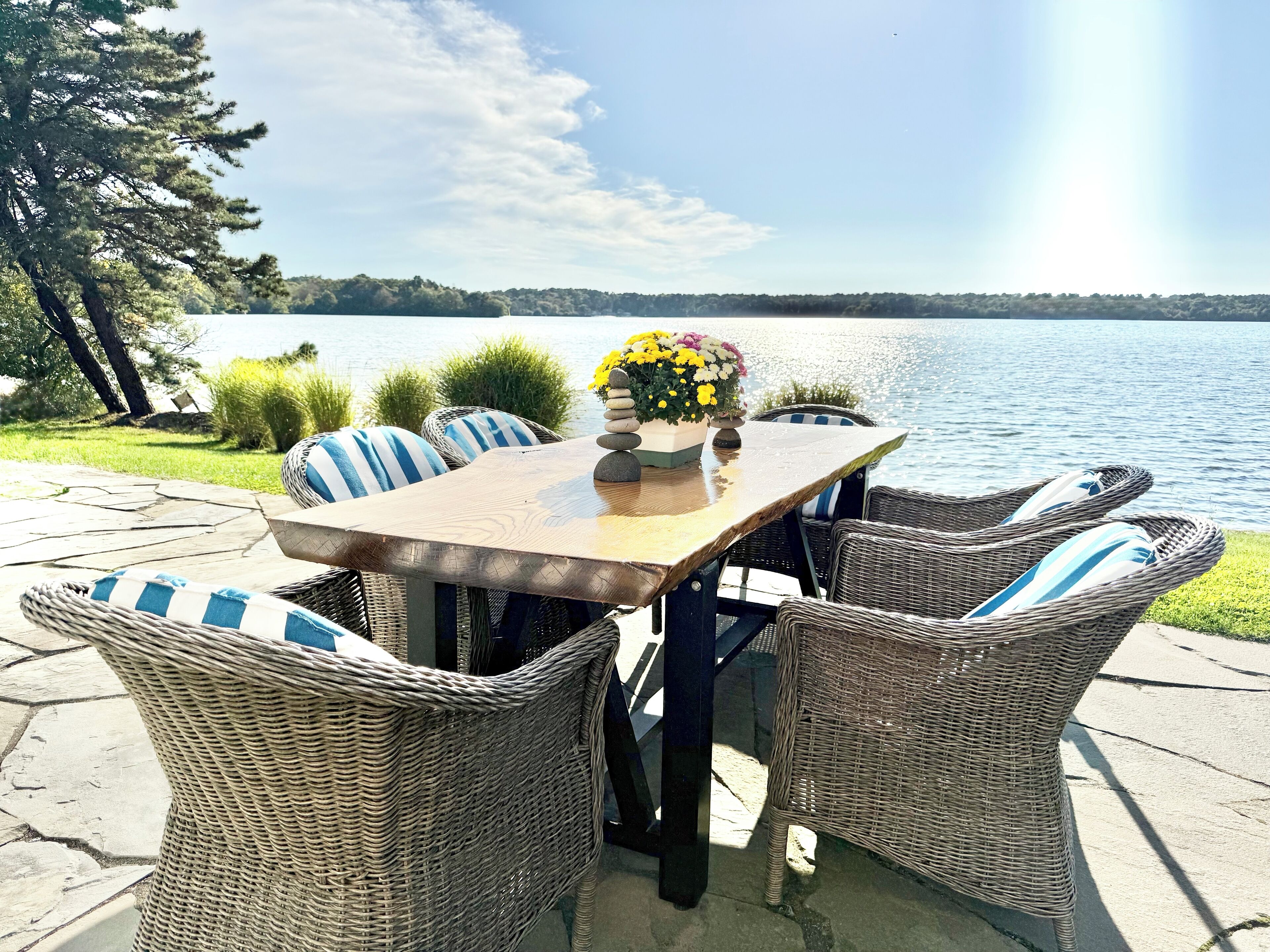 A patio with wicker chairs and a table, overlooking a lake.