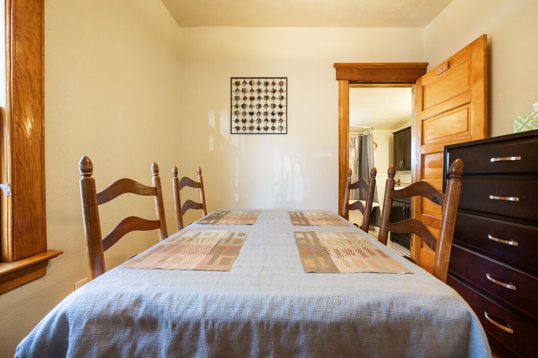 Une salle à manger avec une table dressée pour quatre personnes, des chaises en bois, un buffet en bois et un tableau accroché au mur.