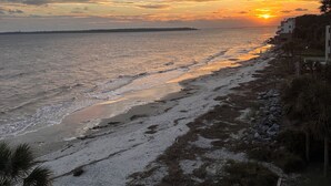 A beach with a sunset, a rocky shoreline, and a building with a balcony overlooking the sea. - Newly Renovated Oceanfront Condo • Right on the Beach • Beachfront • Great Views (Saint Simons Island)