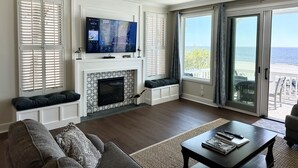 A living room with a fireplace, a television, and a view of the ocean. - Newly Renovated Oceanfront Condo • Right on the Beach • Beachfront • Great Views (Saint Simons Island)