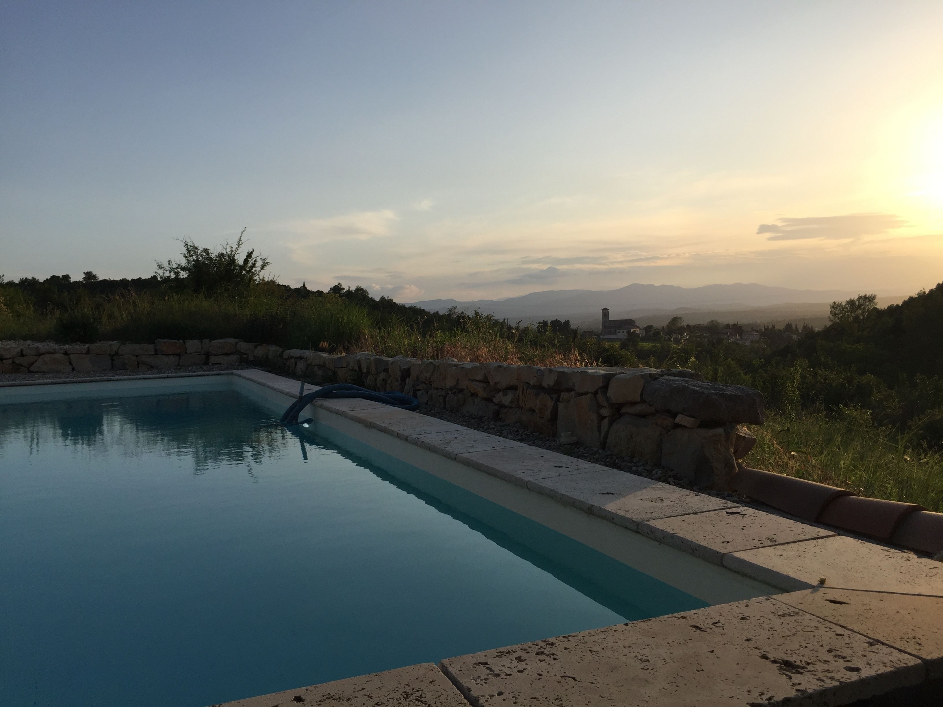 A swimming pool with a stone border, surrounded by greenery and a view of distant mountains.