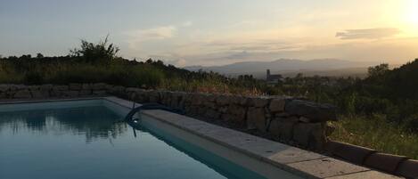 A swimming pool with a stone border, surrounded by greenery and a view of distant mountains.
