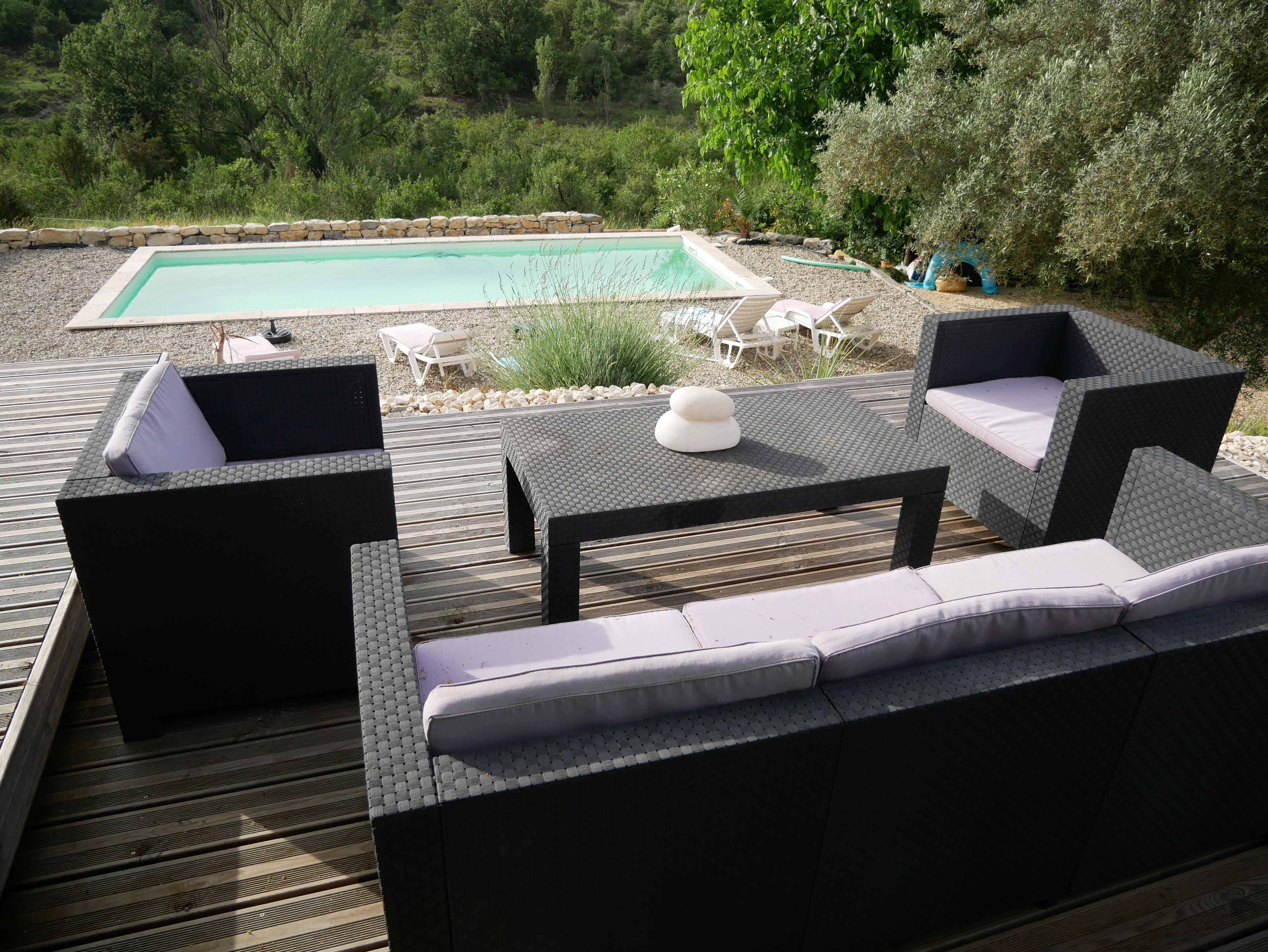 Une terrasse extérieure avec une piscine, des meubles en osier et un mur en pierre.