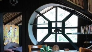 A rustic dining area with a large wooden table centered on a tree stump base, surrounded by wooden chairs. - Treetop House - Charming Artistic in the Canopy of Monteverde (Monteverde)