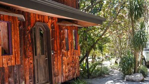A rustic wooden building with a wooden door and windows, surrounded by greenery and a stone pathway. - Treetop House - Charming Artistic in the Canopy of Monteverde (Monteverde)