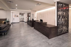 Un área de recepción moderna con un mostrador oscuro, zona de estar con un sofá y sillones, y una pared decorativa con un diseño geométrico.