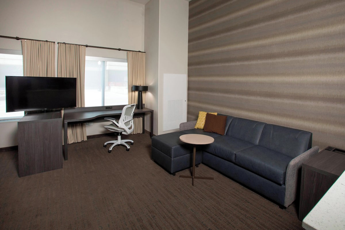 A hotel room with a large flat-screen TV, a desk with a chair, a sofa, and a small round table.