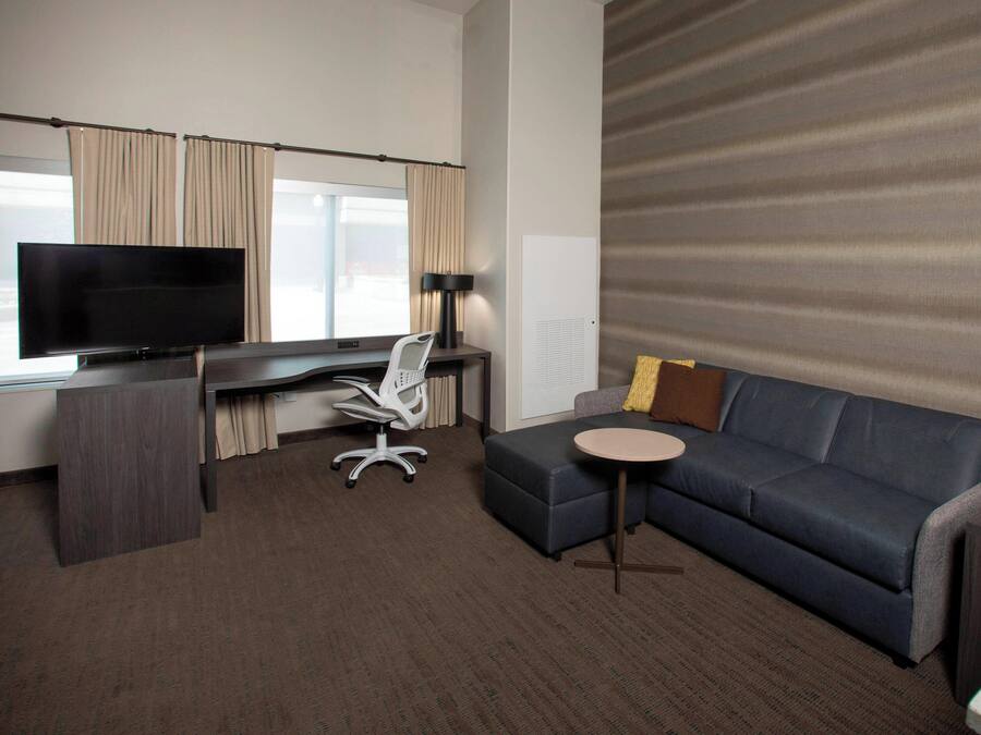 Habitación de hotel con una gran televisión de pantalla plana, un escritorio con una silla, un sofá y una pequeña mesa redonda.