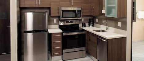 A modern kitchen with stainless steel appliances, wooden cabinets, and a white countertop.