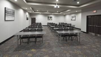 A conference room with tables and chairs arranged for meetings, a projector on the ceiling, and an exit sign on the wall.