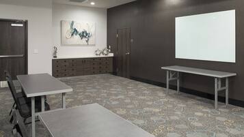 A conference room with a large projection screen, a whiteboard, and a seating area with tables and chairs.