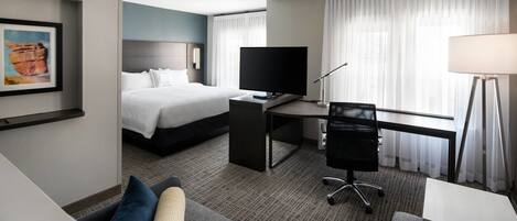 A hotel room with a bed, a desk with a TV, a chair, a lamp, and a couch.