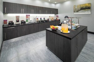 Una cocina moderna con armarios oscuros, una isla central con un cuenco de frutas y dispensador de bebidas, y diverso equipo para preparar alimentos.