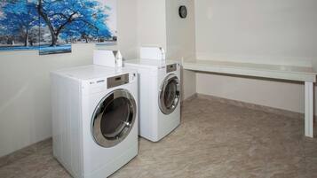 A laundry room with two white front-loading washing machines, a white bench, and a wall-mounted clock.