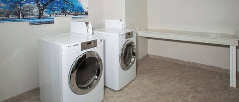 A laundry room with two white front-loading washing machines, a white bench, and a wall-mounted clock.