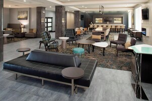 Un hall de hotel con un sofá, sillas, mesas, una zona de bar y una televisión.