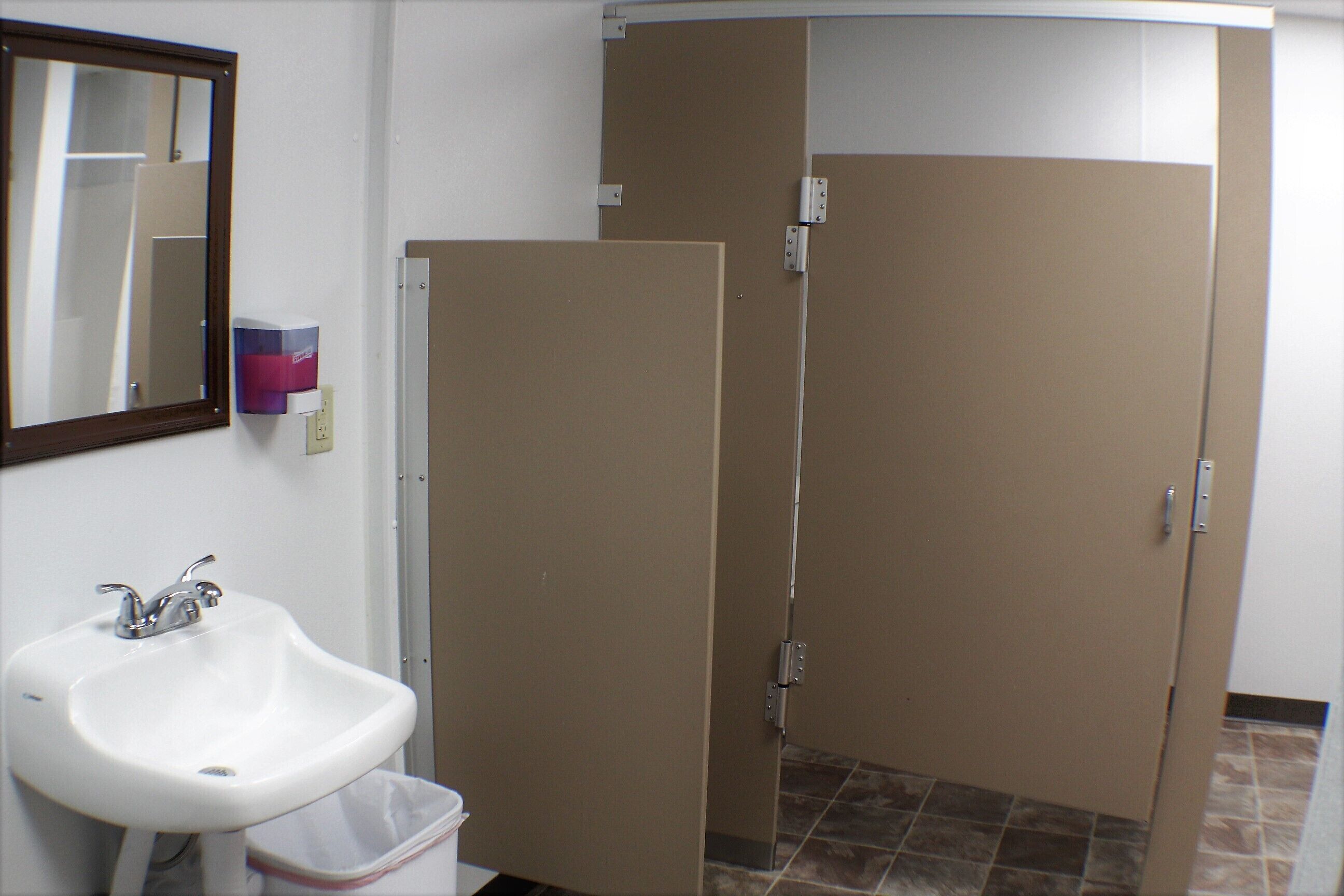 Une salle de bain avec un lavabo blanc, un miroir et deux cabines de douche marron.
