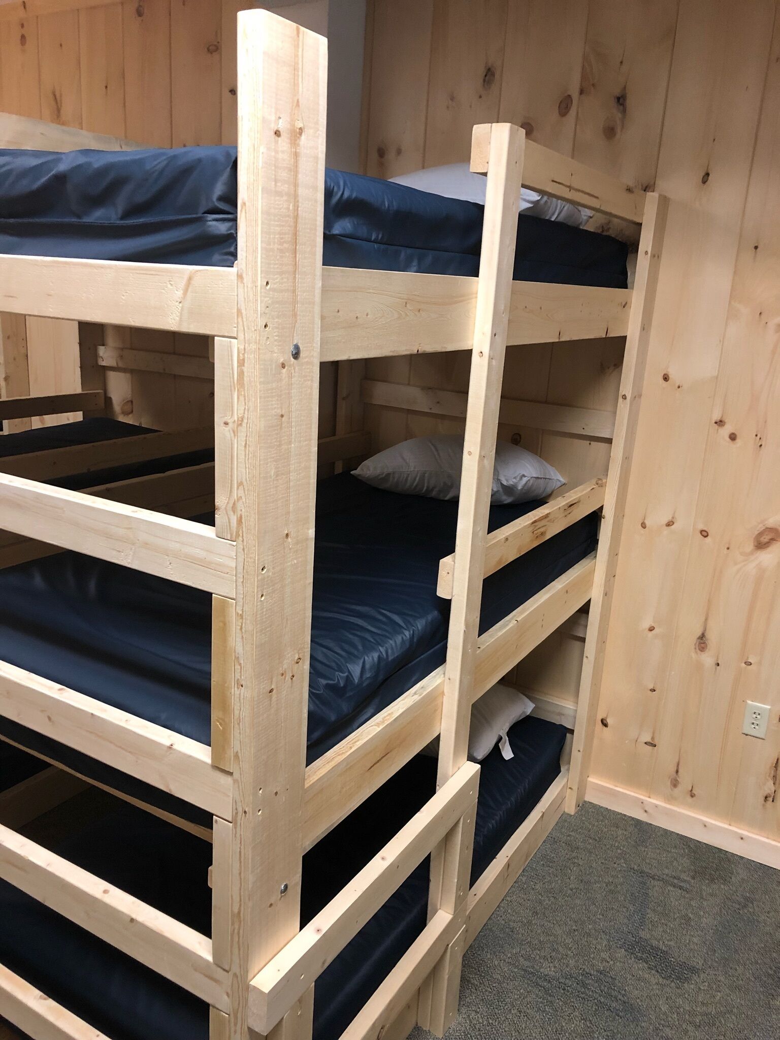 A bunk bed with three levels, wooden walls, and a carpeted floor.