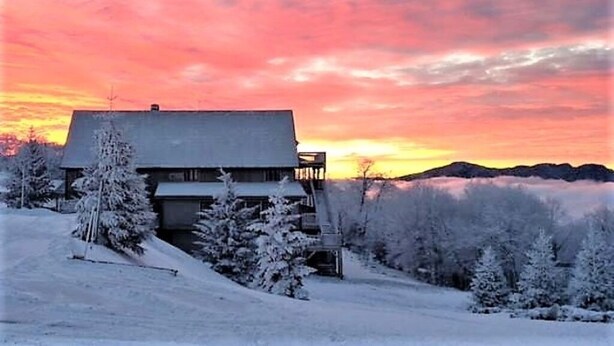 A snow-covered landscape with a house and trees, set against a sunset sky. - Large Group bunkroom sleeps up to 69 (Beech Mountain)