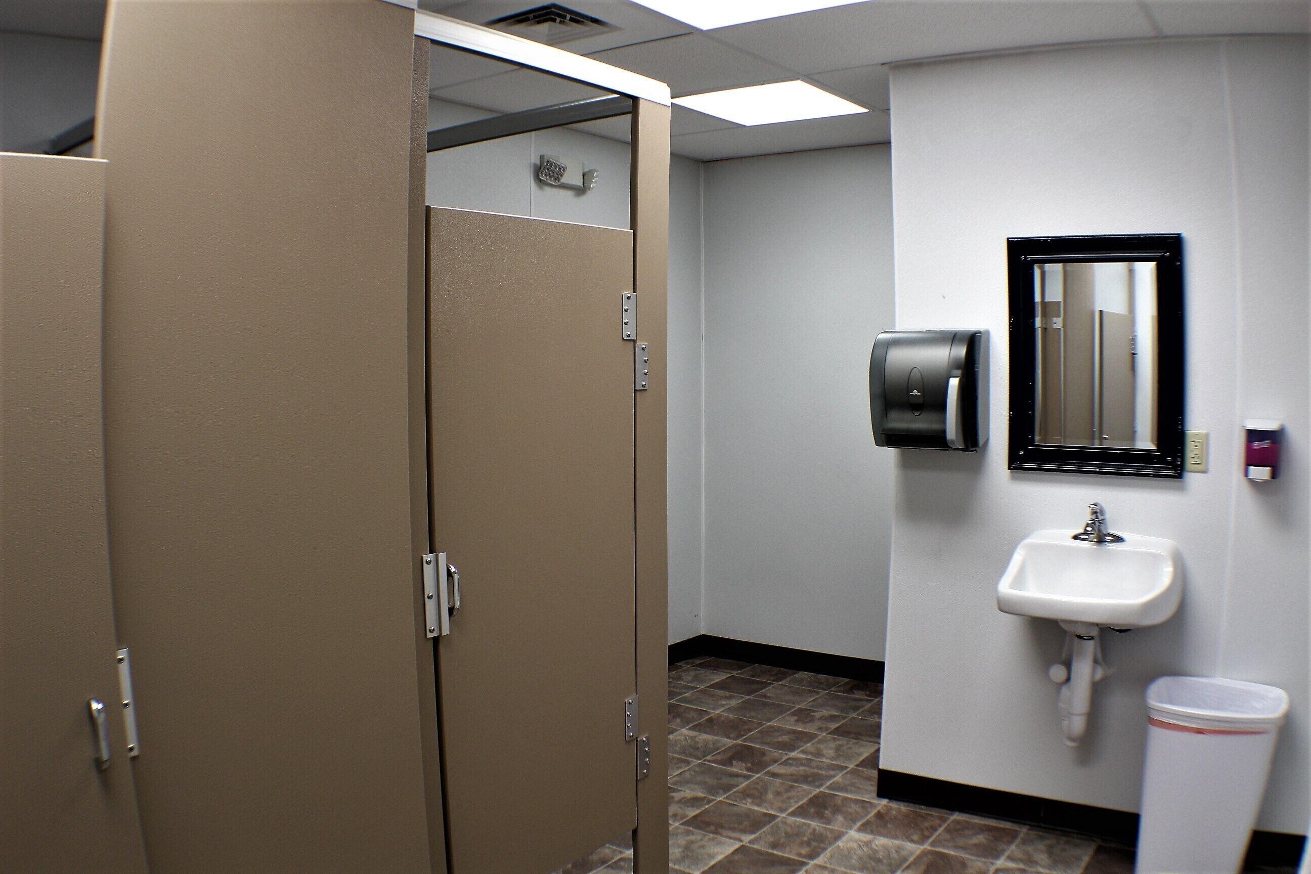 A restroom with two stalls, a sink, a hand dryer, and a trash can.