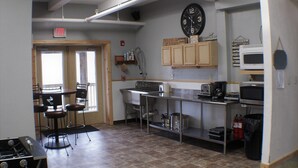 A kitchen with a sink, stove, microwave, and a clock on the wall. - Large Group bunkroom sleeps up to 69 (Beech Mountain)