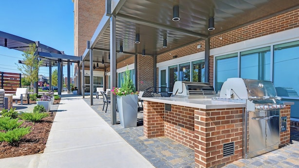 An outdoor patio area with a brick barbecue station, seating, and a covered walkway. - TownePlace Suites by Marriott Jackson Airport/Flowood (Flowood)