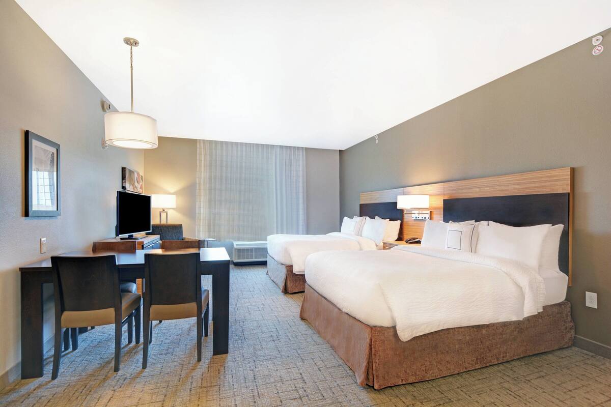 Habitación de hotel con dos camas, un escritorio, sillas y un televisor.