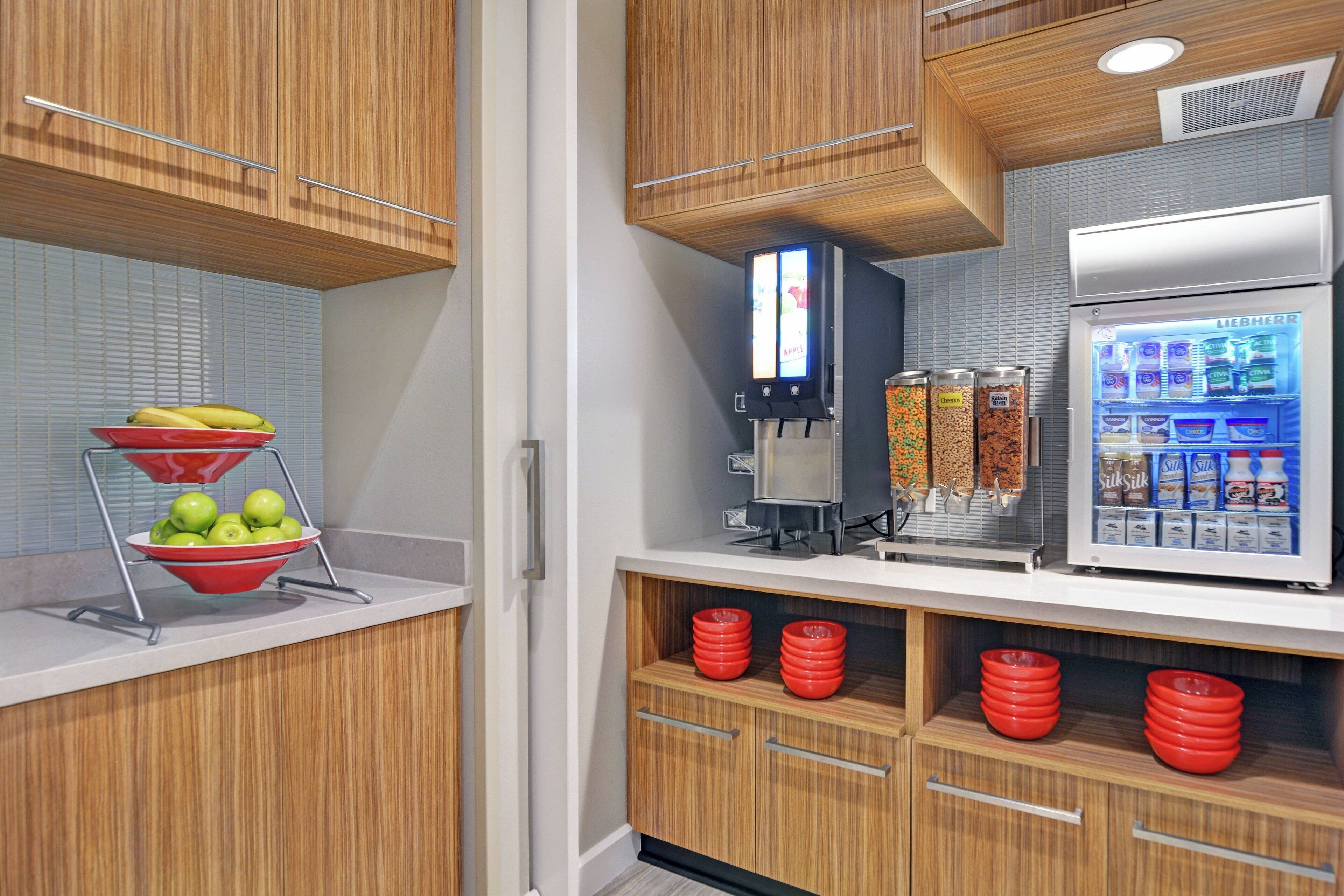 A kitchen with wooden cabinets, a fruit bowl, a coffee machine, and a refrigerator with a beverage dispenser.