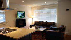 A modern living room with a kitchen island, a fireplace, a television, and a large window with blinds. - Perfect Kitsilano Location - 1 Bed. -1.5  Bath. (for 3 Bed. option see #430414) (Vancouver)