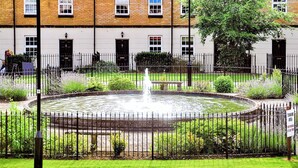 A circular fountain with a bench in the center, surrounded by a metal fence and greenery. - Fountains View Apartment (York)