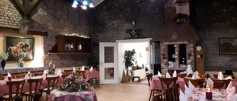 A restaurant with brick walls, wooden beams, and a chandelier. Tables are set with pink tablecloths and white napkins.