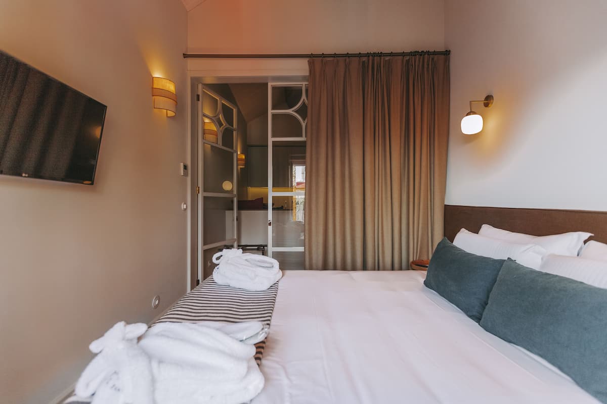 Hotellihuone, jossa on sänky, seinälle asennettu televisio, vaatekaappi ja kylpyhuone, joka näkyy avoimesta ovesta.