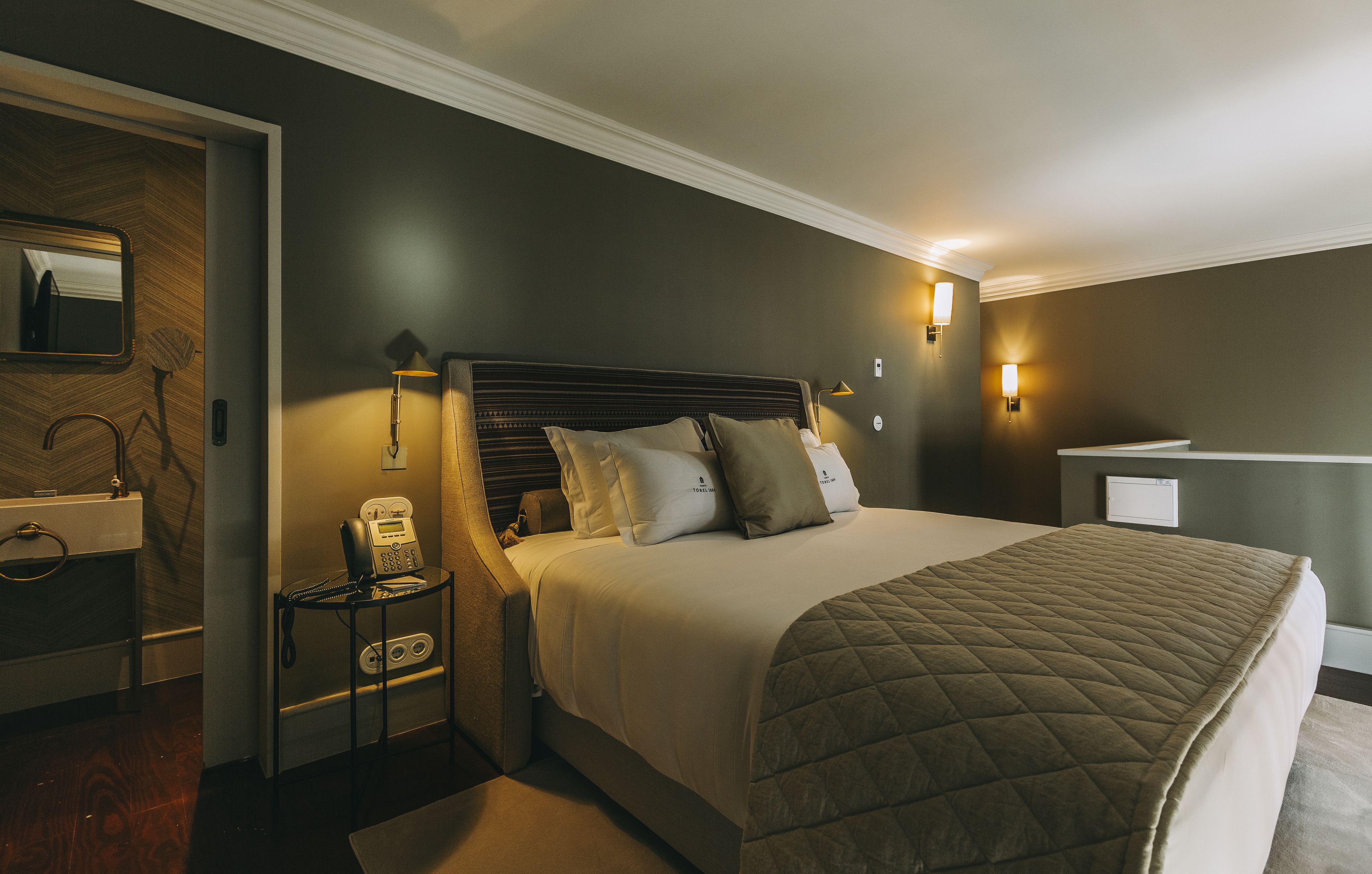 A hotel room with a large bed, bedside lamps, a telephone, and a mirror on the wall.